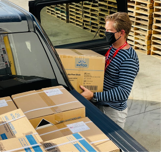 A picture of a man wearing a mask carrying a box into a truck filled it boxes
